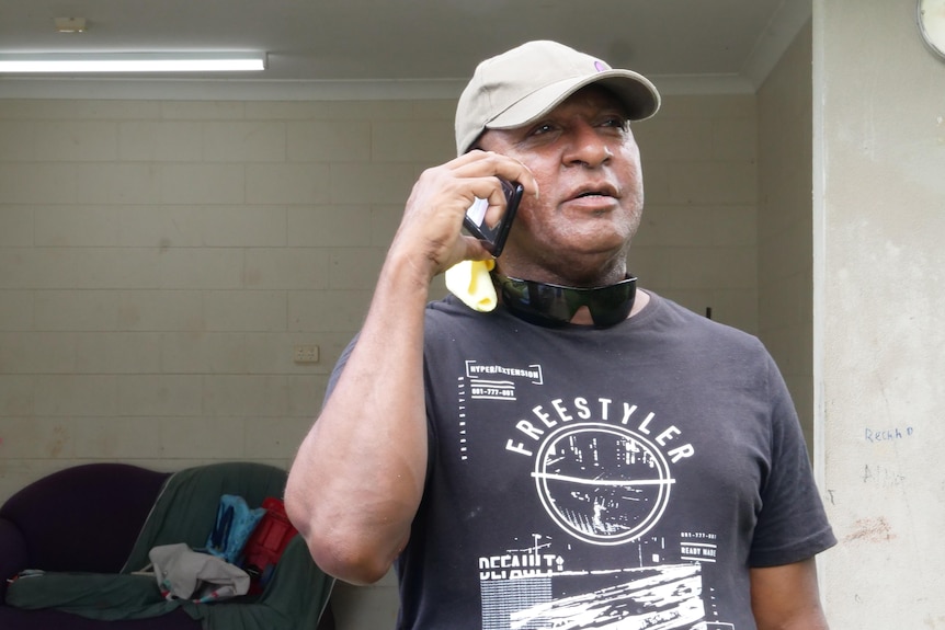 Man holding a mobile phone, wearing a black shirt and a cap.