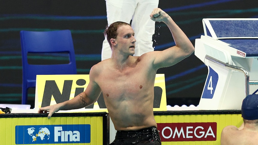 An Australian swimmer sits on the lane rope and pumps his fists in celebration. 