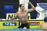 An Australian swimmer sits on the lane rope and pumps his fists in celebration. 