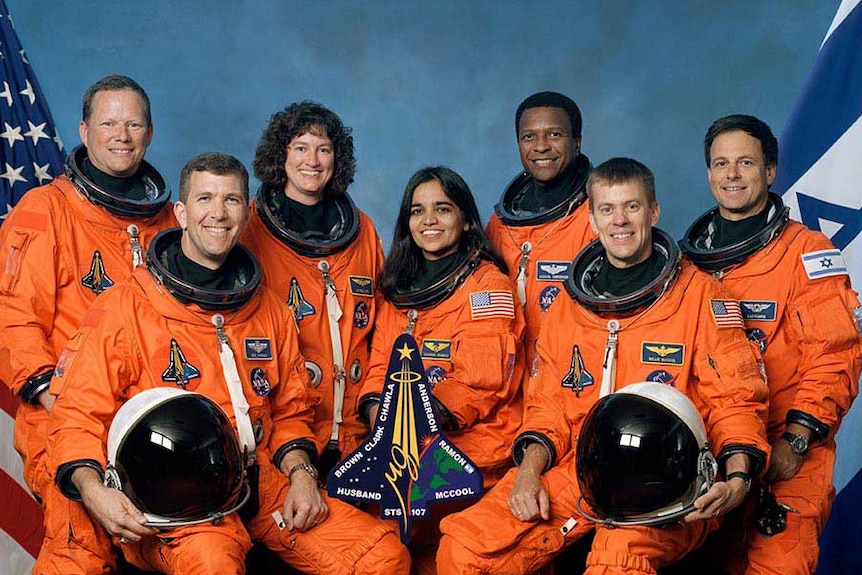 Dwie kobiety i pięciu mężczyzn z załogi promu kosmicznego Columbia nosi pomarańczowe kombinezony lotnicze.