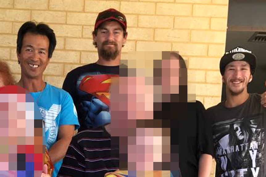 A family photo of three men with name tags above their heads, standing against a light brick wall.