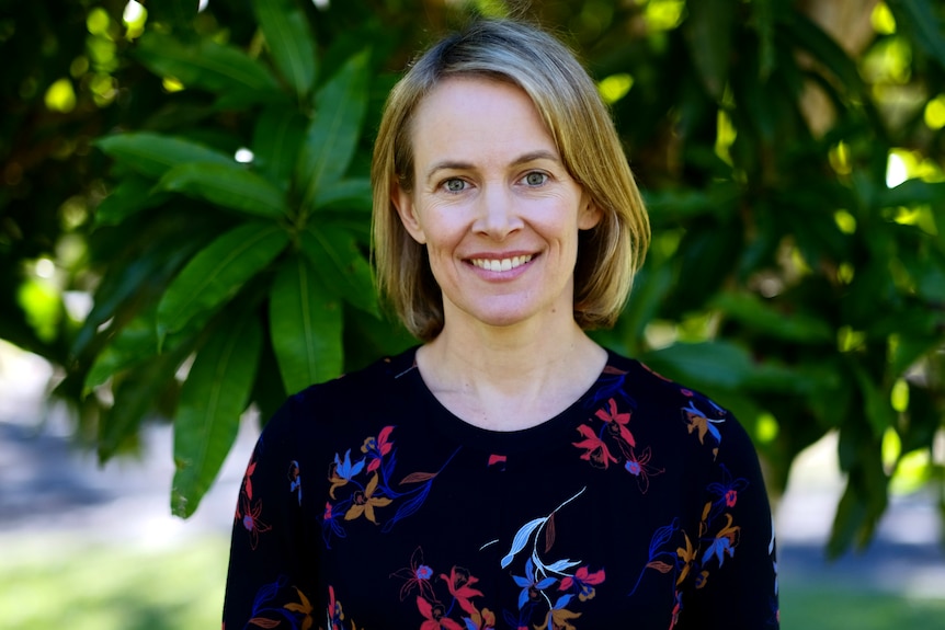 Dr Katharine Kemp smiles at the camera standing in front of a blurred background of green leaves