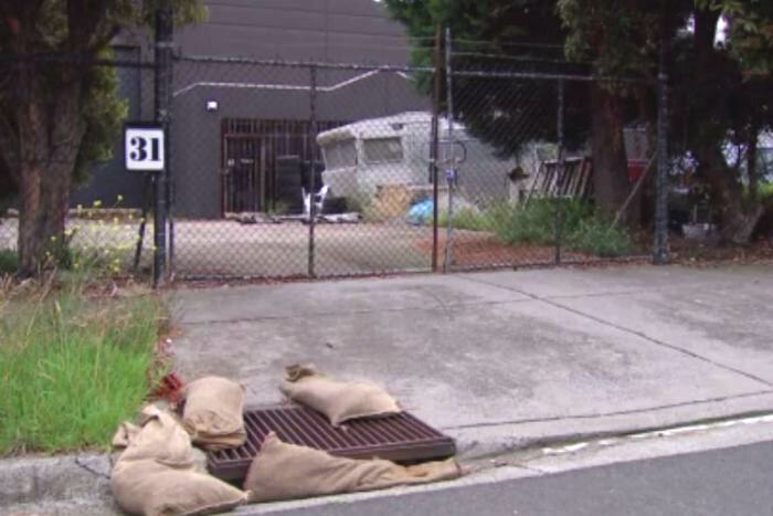Sandbags are placed around a drain outside a derelict-looking warehouse.