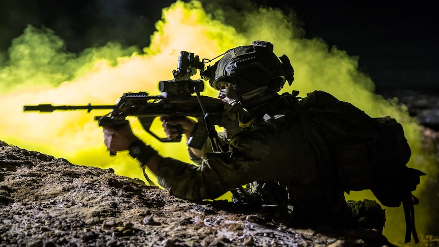 Silhouette of fully armed Australian soldier at night with smoke in backdrop