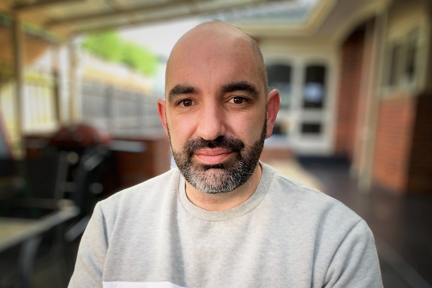 A bald man with a dark beard, wearing a grey sweatshirt.