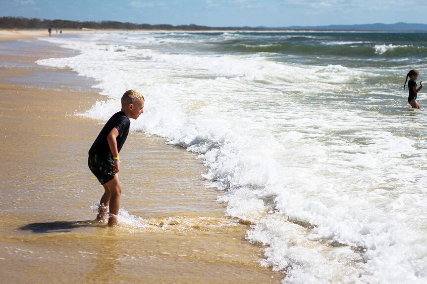 Primary school boy dressed in swimmers prepares to jump waves at Rainbow Beach on Queensland's Fraser Coast.