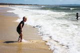 Primary school boy dressed in swimmers prepares to jump waves at Rainbow Beach on Queensland's Fraser Coast.