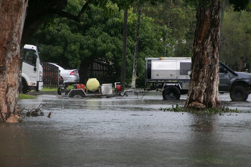 Ute trailer wheel half under water with flooding surrounding the ute. 