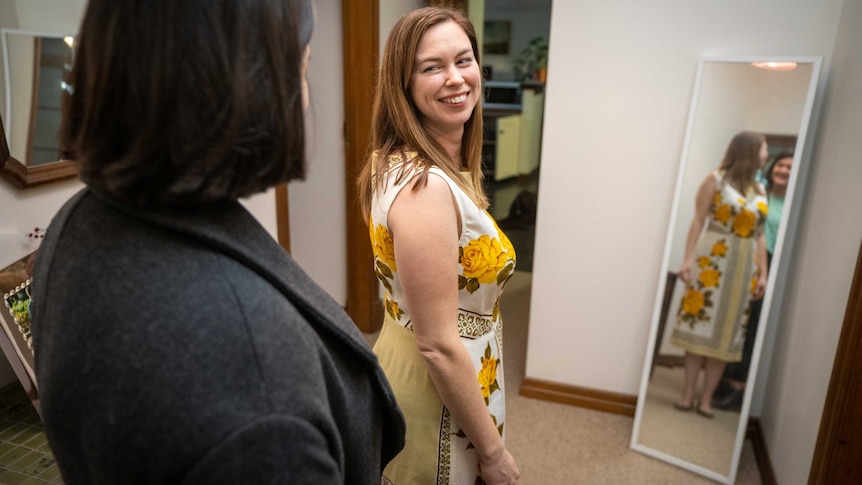 Eleanor Russell standing in the dress in front of a mirror, smiling over her shoulder