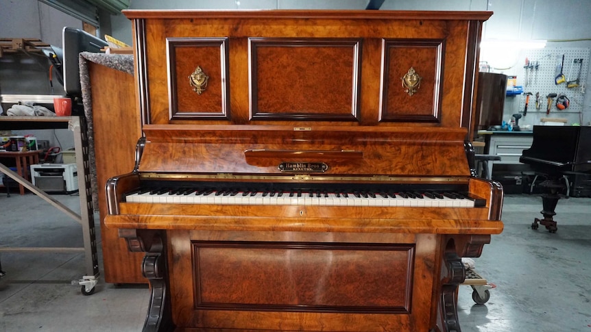 A tan-coloured piano in a warehouse.