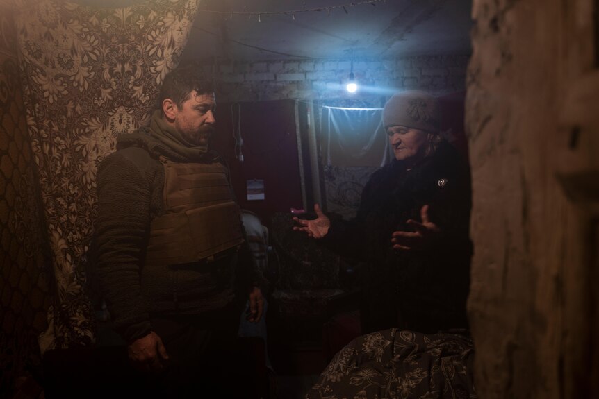 an elderly women gestures while talking to a man in a bunker