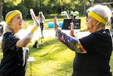 A teen on the left high fives a senior on the right. Both are wearing bright yellow sweat headbands and black shirts