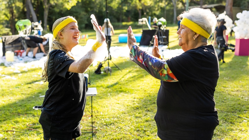 A teen on the left high fives a senior on the right. Both are wearing bright yellow sweat headbands and black shirts