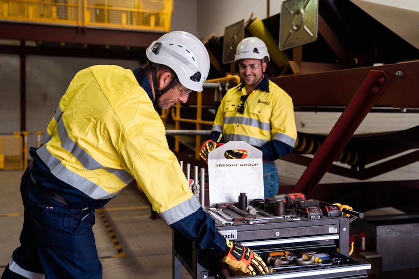 Two men in high-vis clothing and helmets stand near a toolbox.