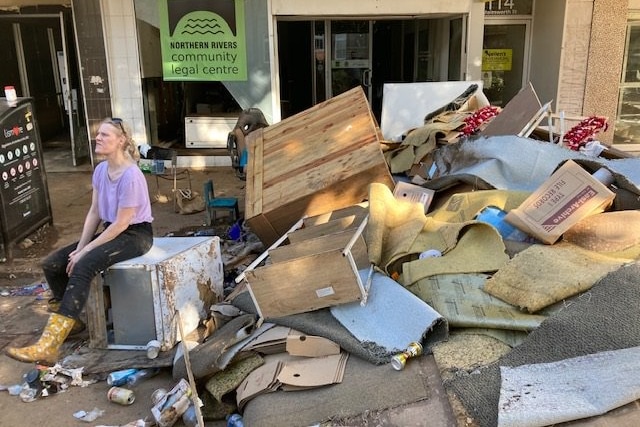 A woman stares off into the distance, sitting amongst the rubble of junk cleared from her office