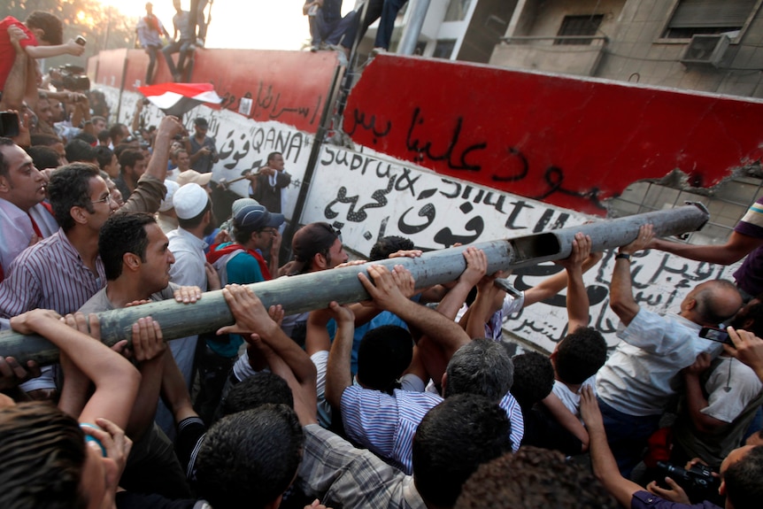 Protesters knock down a concrete wall built in front of the Israeli embassy in Cairo