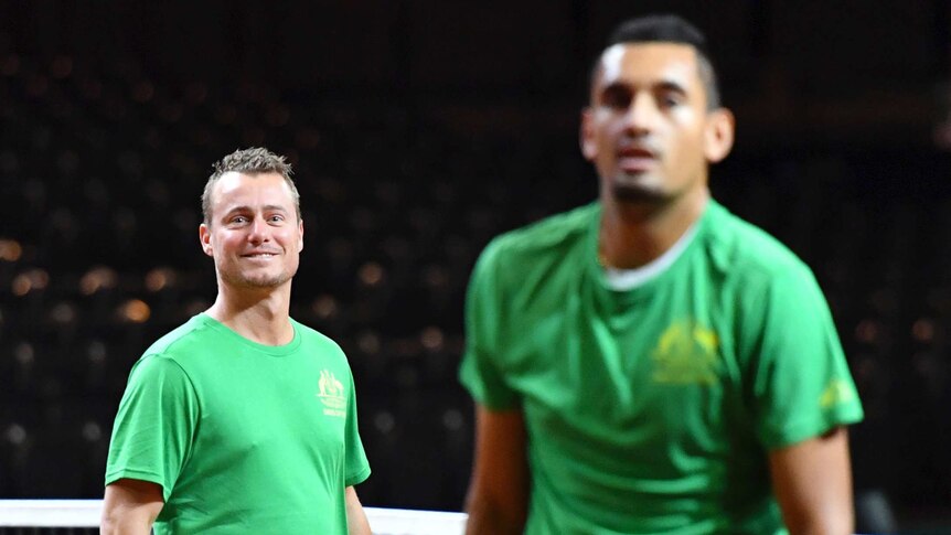 Lleyton Hewitt watches Nick Kyrgios, blurred in the foreground.