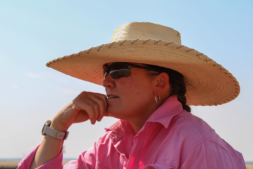 A woman in a hat and sunglasses looks out over a rural property.