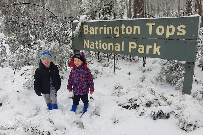 Kids in frolic in the snow in front of a sign for Barrington Tops National Park.