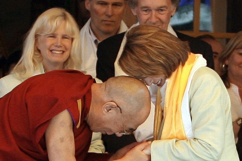 The Dalai Lama in his distinctive deep orange robes bows deeply as a red-haired Ms Pelosi bows, her face touching his scalp