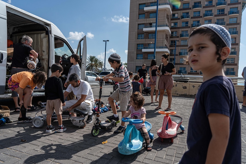 A group of children play with bikes and trikes outside a van in a carpark.