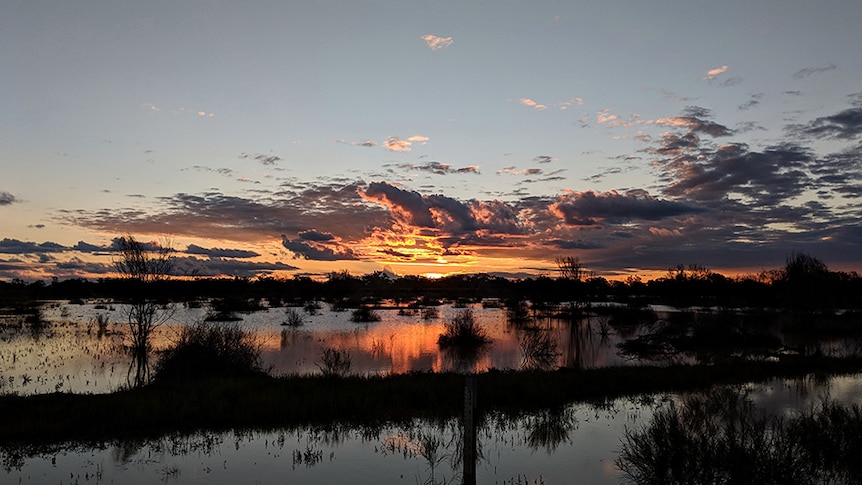 The orange glow of a sunset filtering through clouds in outback western Queensland