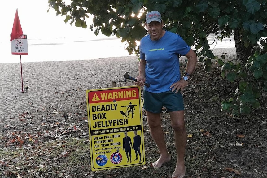 man hammering in beach box jellyfish warning sign. 