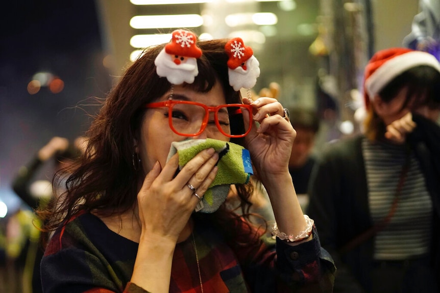 A woman wearing Christmas decorations and red glasses covers her mouth.