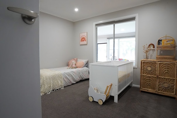 A neatly made bed and cot sit next to each other in a bright, spacious room with toys and books.