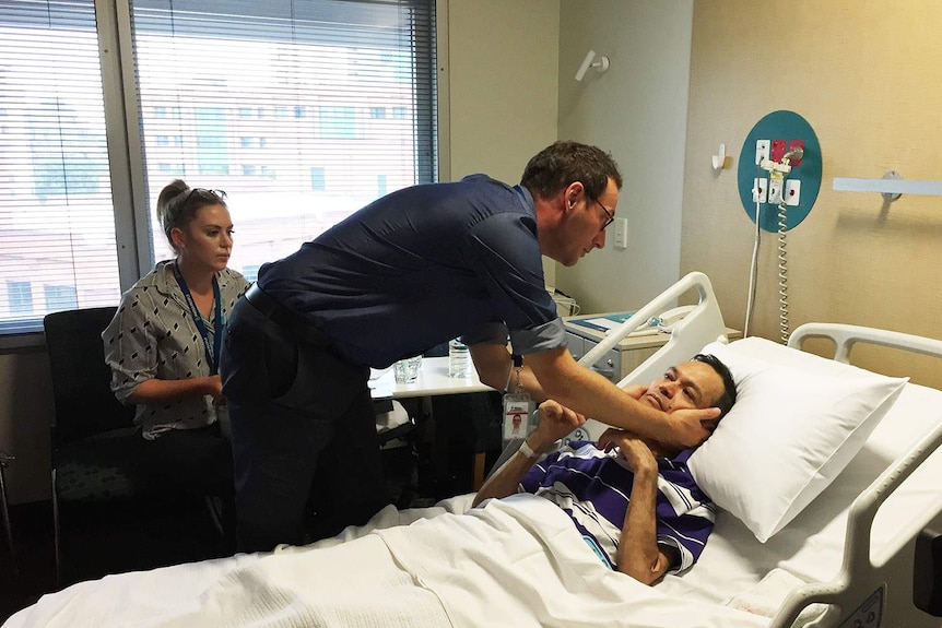 A doctor checks Gerhard Infante as he lies in a hospital bed