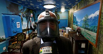 A man in a gas mask in a blue room painted with clouds.