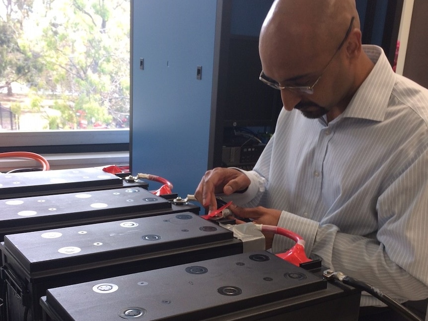 Dr Anand Bhatt from the CSIRO connecting batteries on a table with a cable.