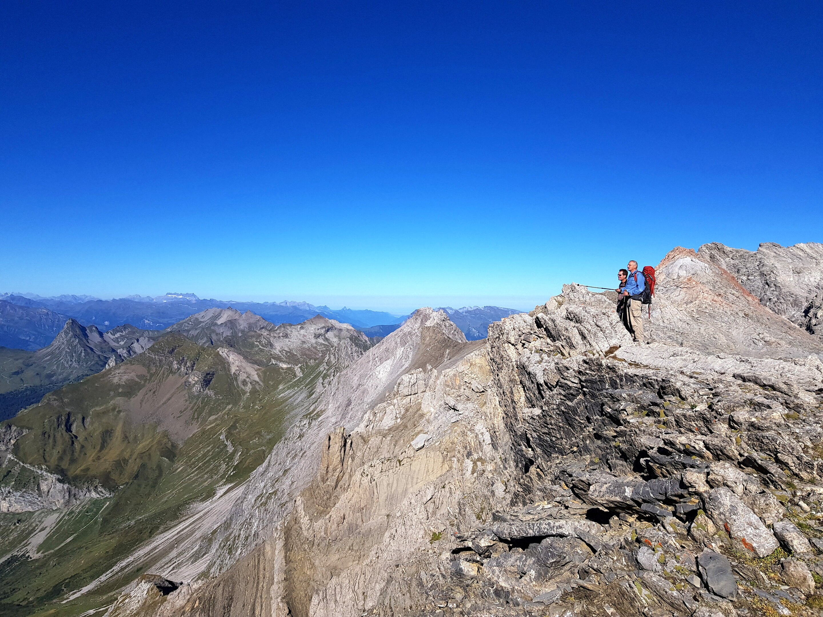 Two men stand atop a mountain overlooking an impressive range that extends way into the distance