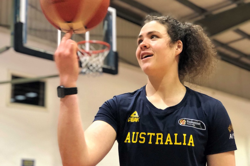 A young woman watches a basketball spin on her index finger