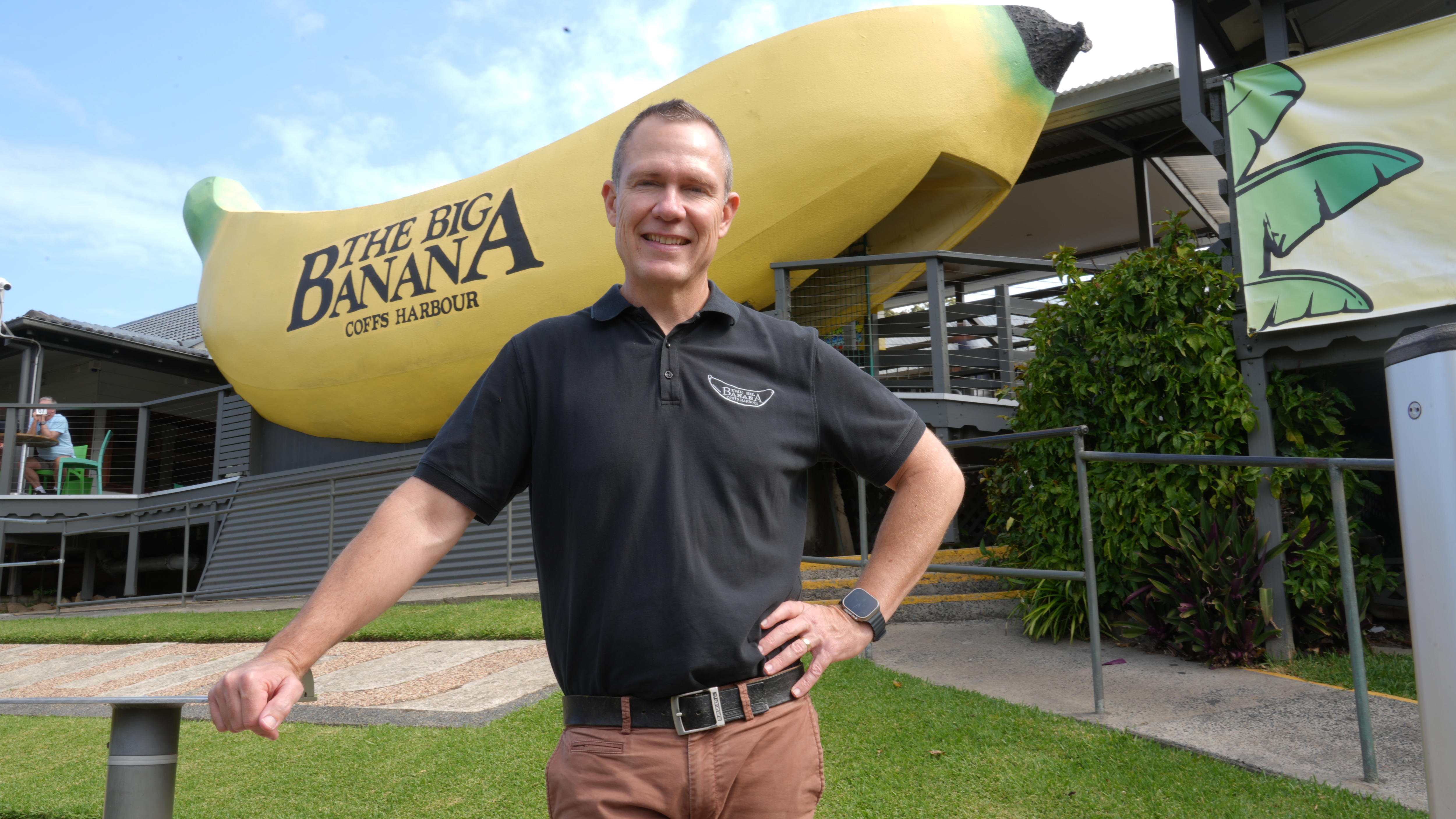 A man in a black polo shirt with Big Banana logo stands in front of the Big Banana.