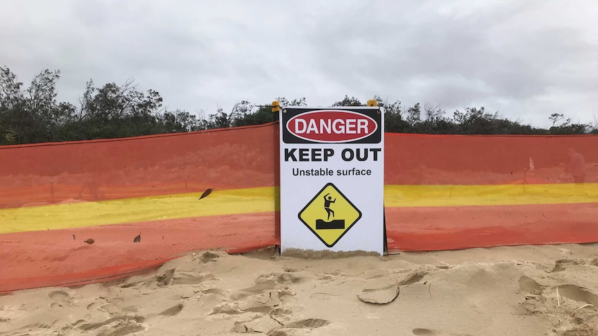 A beach dune with barricade around it and a 'danger keep out' sign