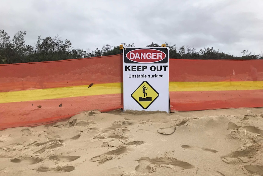 A beach dune with barricade around it and a 'danger keep out' sign