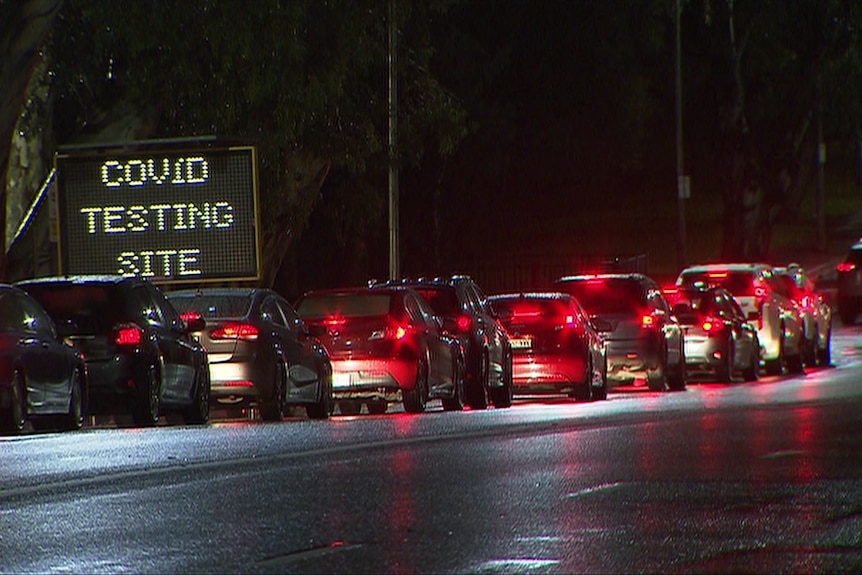 Cars lined up on a road with a sign saying COVID TESTING SITE