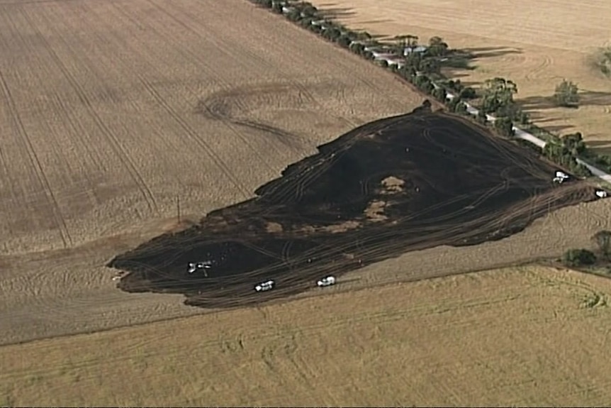 A birds eye view from a distance of a charred paddock with plane debris 