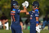 Yastika Bhatia and Shafali Verma high-fove each other while on the field, wearing their batting gear