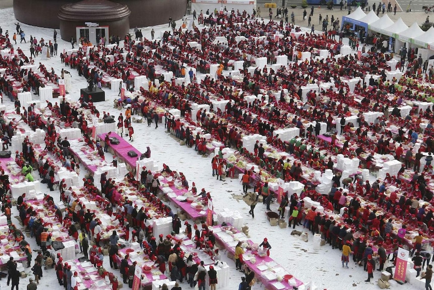 Thousands of people wearing red are making kimchi.