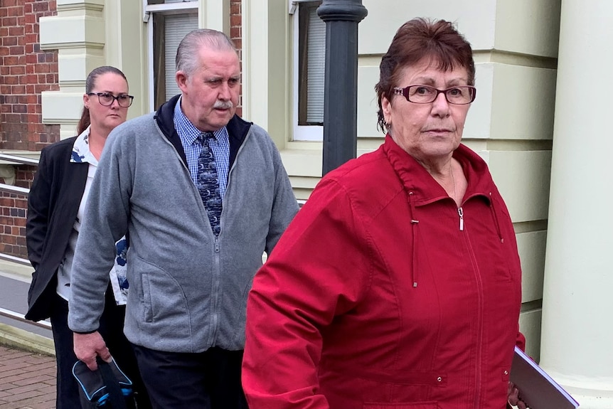 A woman in a red sweater looks at the camera as she leaves a court building followed by a man and another woman