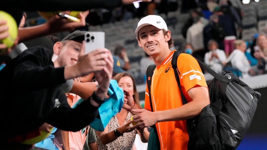 Tennis player Alex de Minaur poses for a selfie with a fan courtside at the Australian Open.