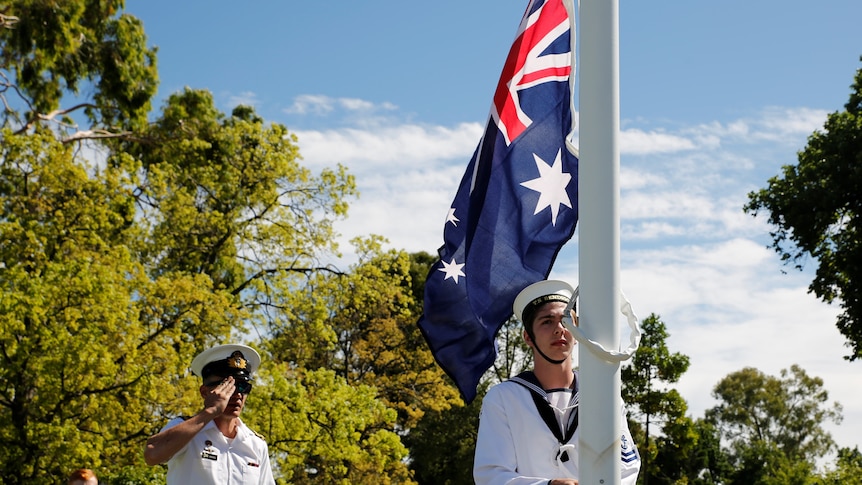 A member of the Australian Navy hoists the Australian flag