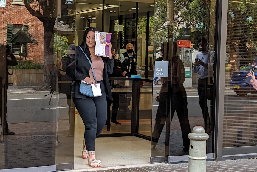 A woman covers her face with a book as she leaves the automatic doors of a court house