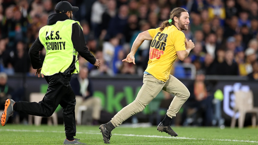 A pitch invader is chased by a security ground on a football field