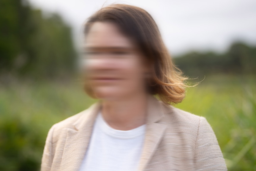 An unidentifiable woman stands with a green park behind her.