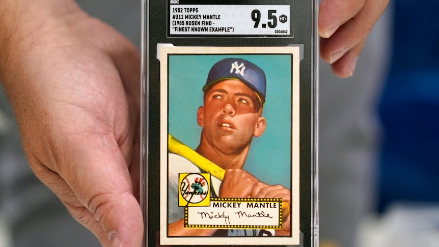 A man holds a baseball card featuring Mickey Mantle