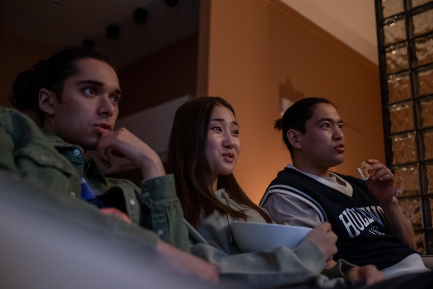 Three friends watching a scary movie on the couch at home