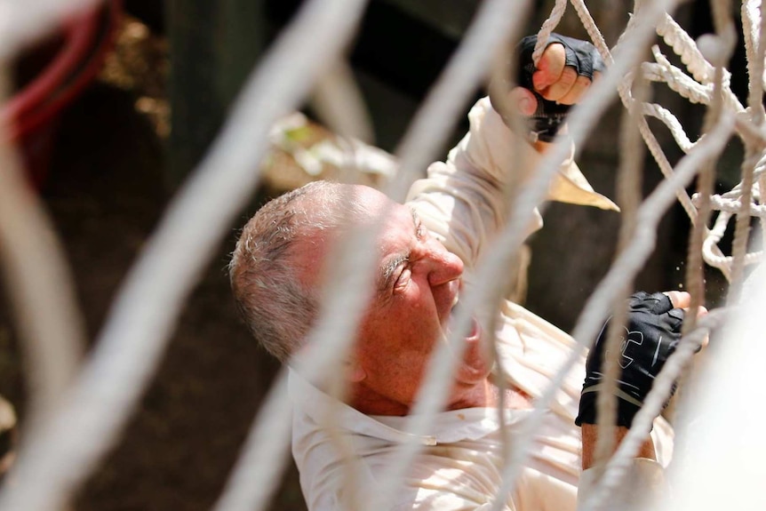 Dave Holleran, seen through wide netting, screams as he climbs a series of ropes.